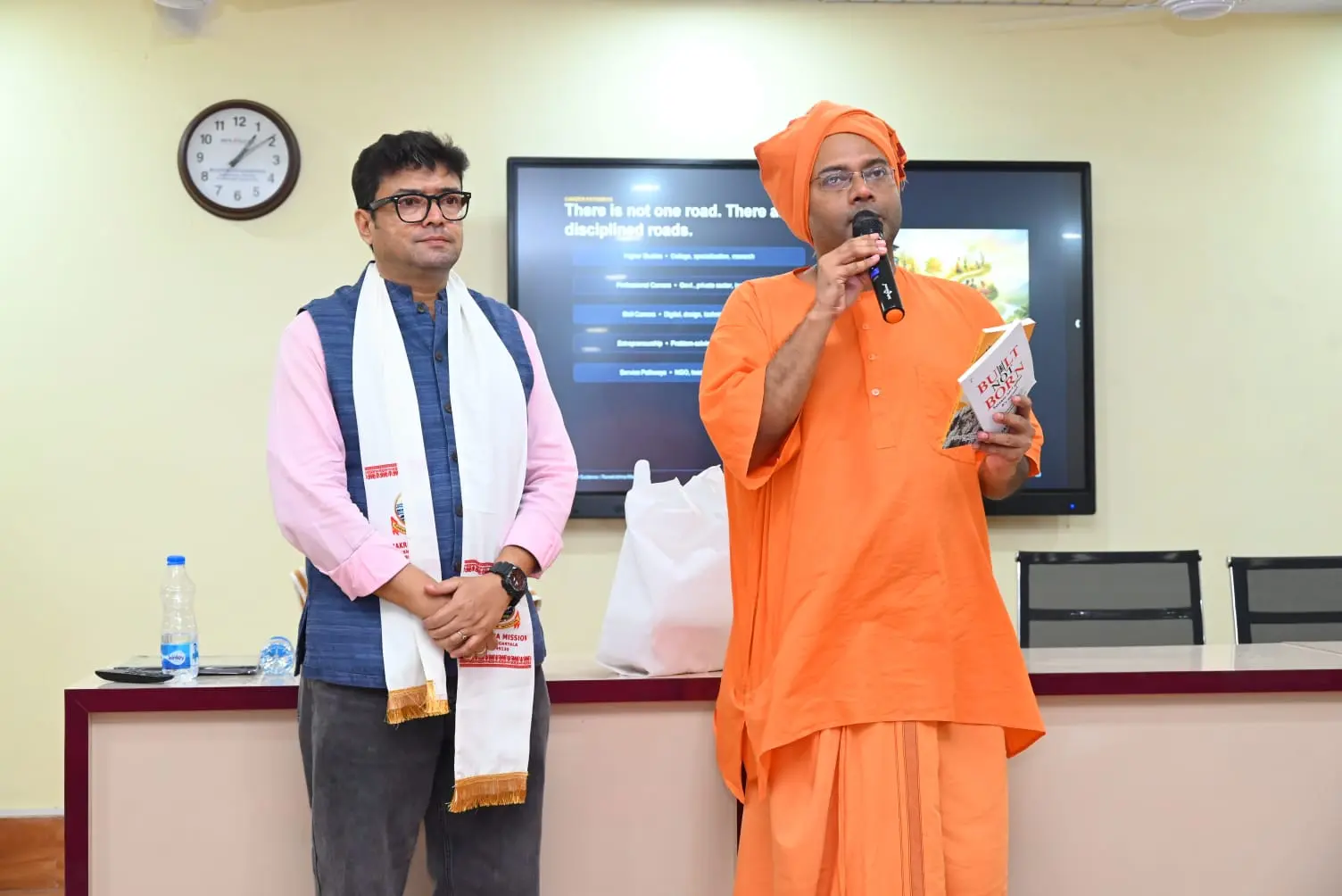 Dr. Jayanta Ghosh introducing the book Built Not Born alongside a monk during a session at Ramakrishna Mission, Agartala
